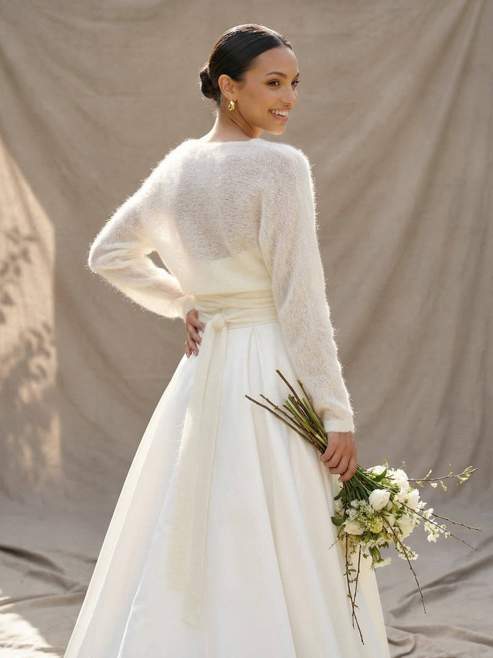 Mariée de dos, cache-cœur en mohair ivoire croisé dans le dos, bouquet à la main