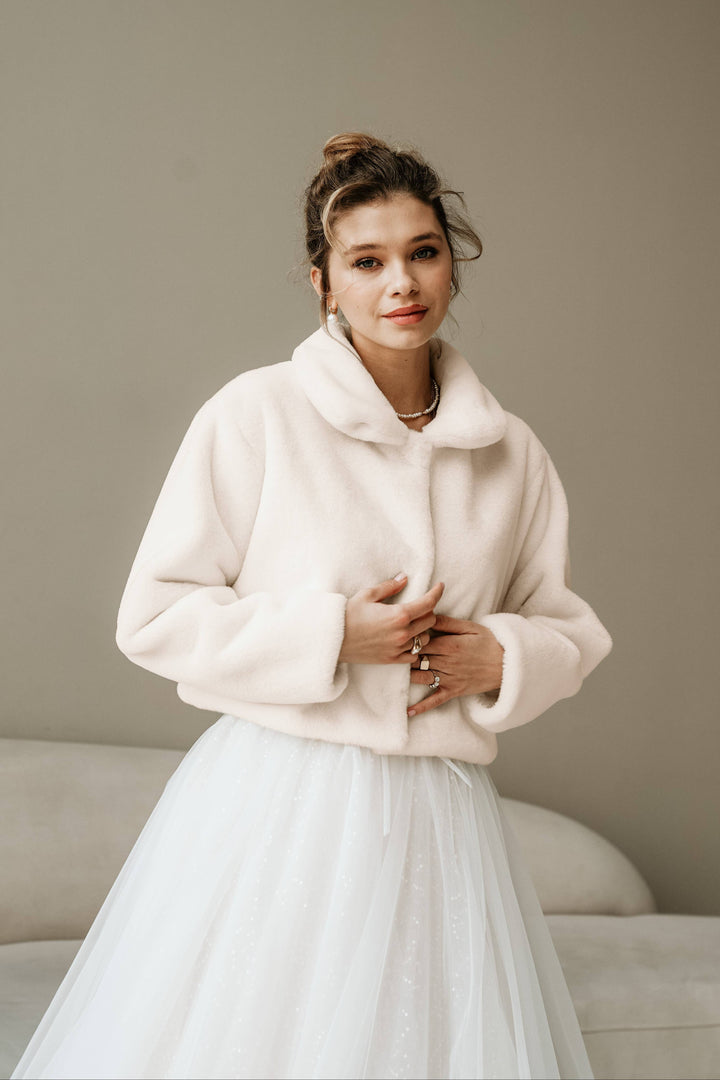 Manteau de fausse fourrure ivoire porté sur une robe de mariée en tulle