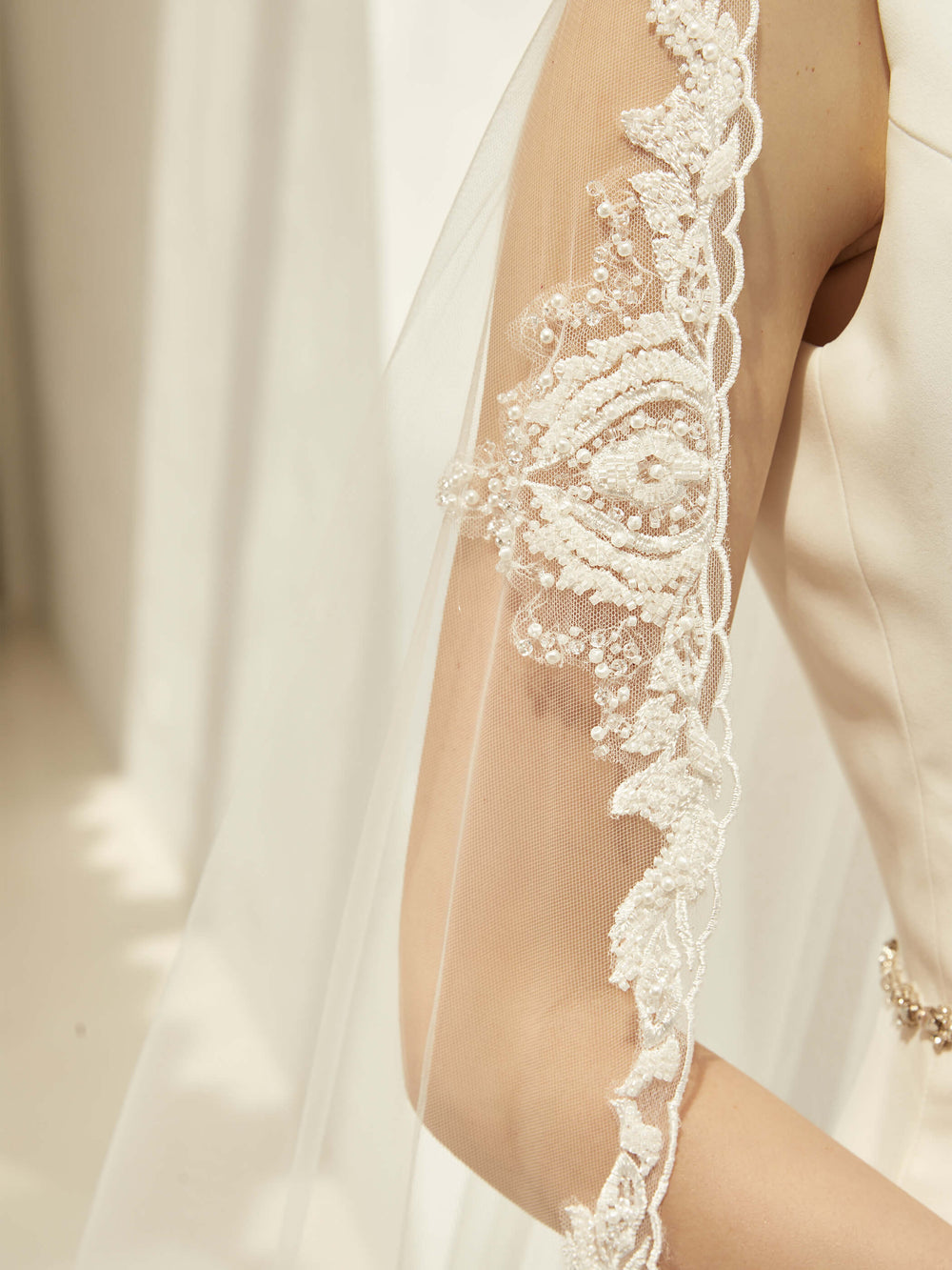 Détail de la bordure en dentelle festonnée brodée et semée de perles du voile de mariée S423 Bianco Evento