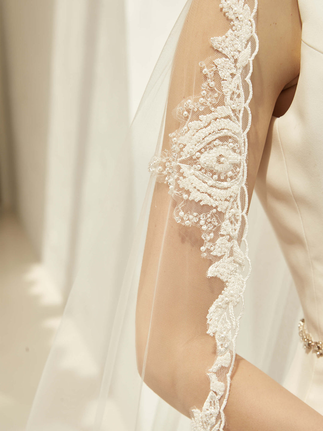 Détail de la bordure en dentelle festonnée brodée et semée de perles du voile de mariée S423 Bianco Evento